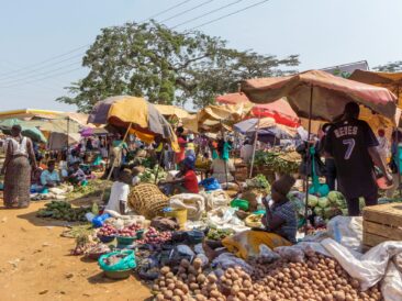 Vendors and buyers at a rural African market, exchanging a variety of fresh produce and goods
